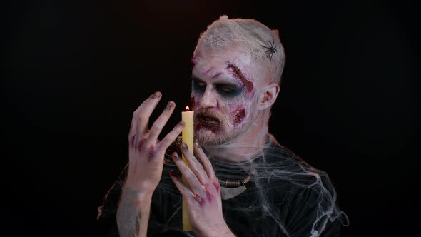 Zombie Man with Makeup with Fake Wounds Scars and White Contact Lenses Spells Conjures Over a Candle