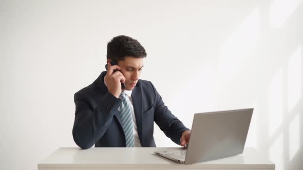 Business Man in Formal Wear Works Sitting Table with Laptop and Talking on Phone