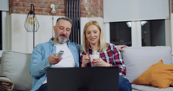Couple Relaxing on the Comfortable Sofa in House and Watching Video on Laptop