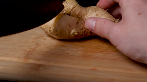 Cutting a ginger tuber on a wooden cutting board.