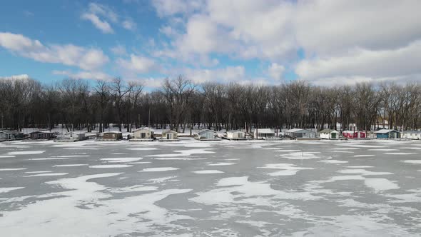 Wisconsin frozen river with house boats lining the shore. Bare trees in the park.