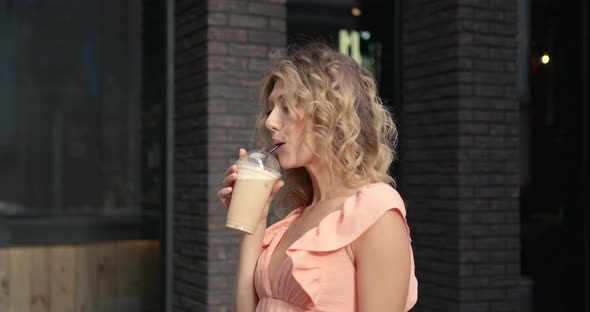 Smiling Woman Standing Outside Drinking a Coffee and Carrying Flowers