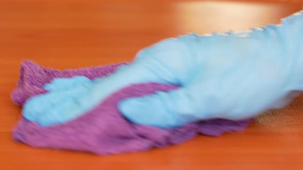 With a close palm, a hand in a medical glove wipes the surface of a wooden table with a rag