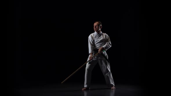 Kendo Fighter on White Kimono Practicing Martial Art with the Bamboo Bokken on Black Background