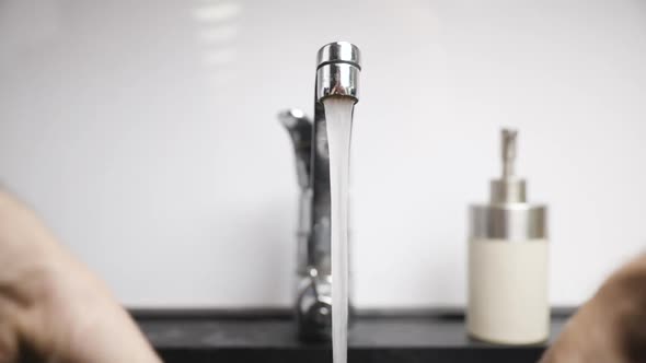 Close-up of male hands being washed with soap by bathroom faucet