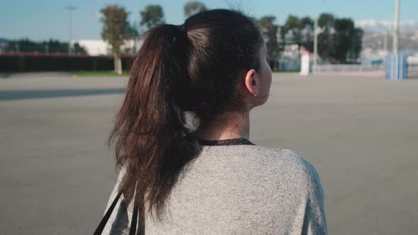 Young Brunette Lady Is Strolling Alone in City in Summer Day, Back View