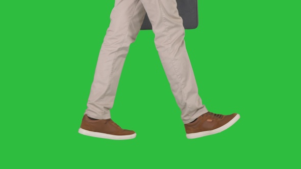 Mans feet is walking in jeans and sneakers on a Green Screen