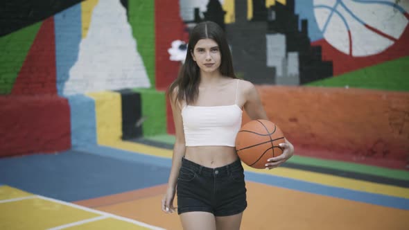 Portrait of Confident Brunette Young Sportswoman Walking with Basketball Ball Looking at Camera