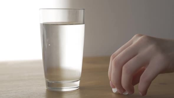 Somebody Takes Glass with Water and Pills From White Table