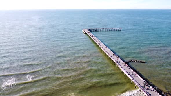 People walking on Palanga bridge on sunny day with calm sea, aerial ascend view