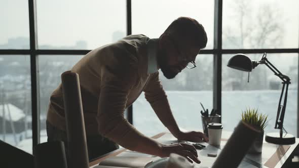 Bearded Man in Glasses Makes Sketches in Front of Large Window