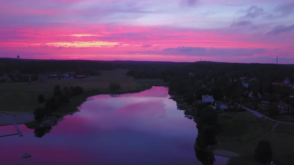 Aerial descending, drone view backwards, above a lake and a town, purple sky, at a colorful sunset o