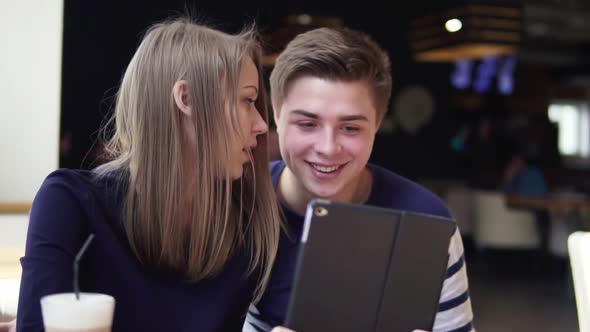 Young Attractive Couple Using Digital Tablet Computer Looking at the Screen in Cafe