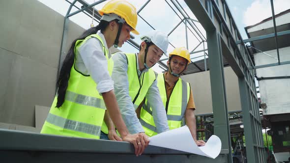 Asian construction workers and builder people holding drawing and working onsite of architecture.