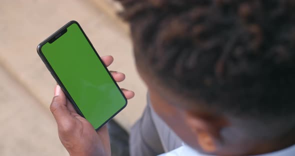 Over Shoulder View of Afro American Guy Sitting and Looking at Phone Green Screen. Man Holding Mock