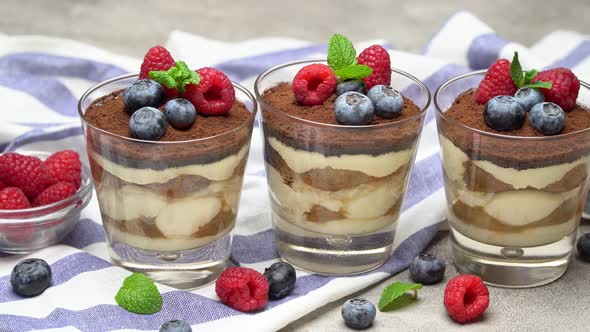 Classic Tiramisu Dessert with Blueberries and Raspberries in a Glass on Concrete Background