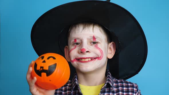 Caucasian boy 7 years old in a carnival costume with makeup on his face in a hat with a pumpkin on a