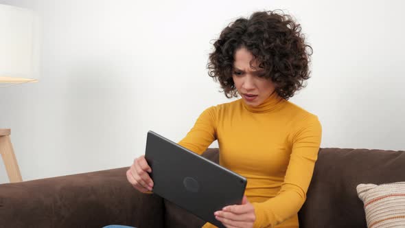 Curly Woman Emotionally Playing Video Game on Tablet Sitting on Couch at Home