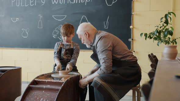Kid Creating Earthenware Using Pottery Wheel in Workshop Under Guidance of Senior Man
