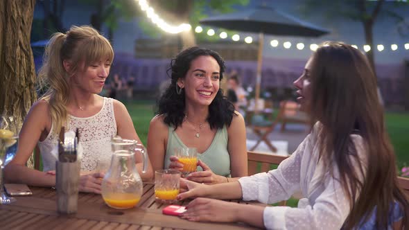 Three Female Friends Sit in the Outdoors Cafe Drink Juice and Have Fun Communicating Laughing in the
