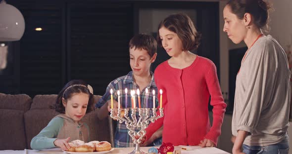 Kids and their mother eating donuts with a menora and dreidels