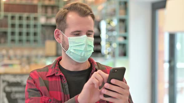 Portrait of Young Man with Face Mask Using Smartphone