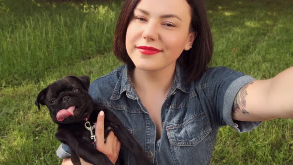 Young woman taking selfie with puppy pug dog using phone. Ttakes a photo with her pet. 