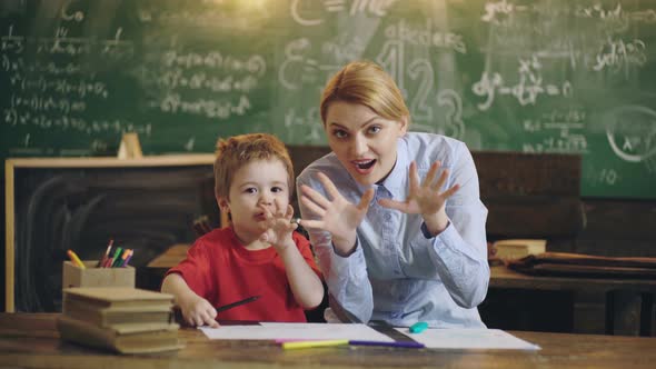 Elementary School Teacher. Mother Helping Kid Boy in School Classroom.