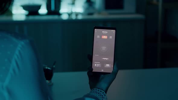 Woman Sitting in House with Automation Light System Holding Smartphone