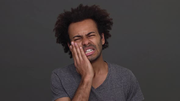 African American Young Man Touching His Cheek Showing Toothache Isolated on Charcoal Background