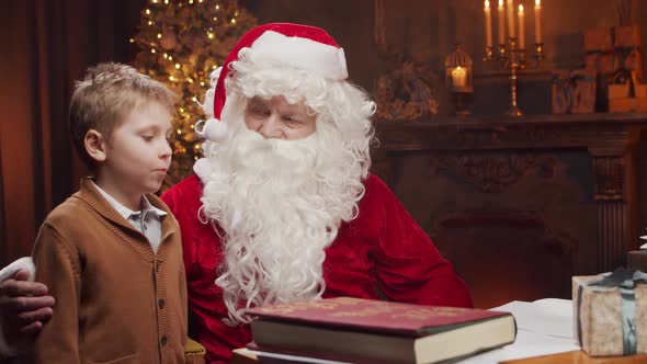 Santa Claus and little boy. Cheerful Santa is working at the table. Christmas concept.