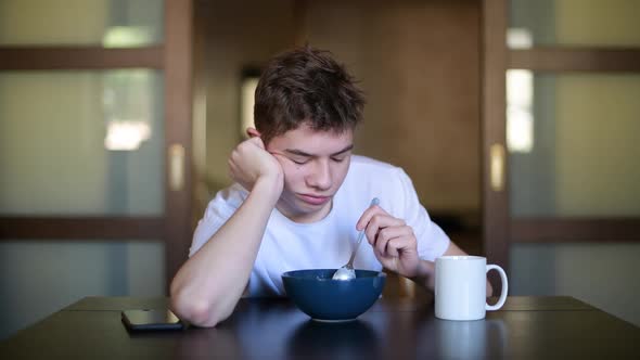 A teenager with a sleepy face picks himself in a bowl of porridge