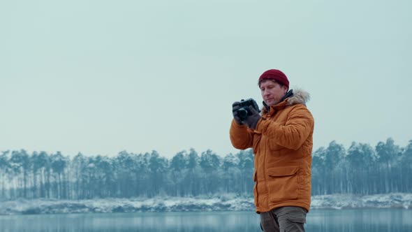 Traveler in an Orange Jacket Takes a Picture with a Modern Camera Against the Background of a Winter