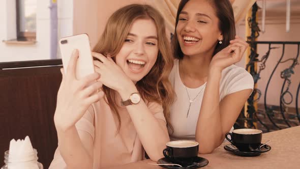 Two young beautiful smiling hipster girls chatting in cafe