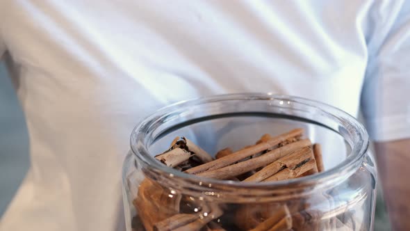 Woman with a Glass Jar of Cinnamon Sticks at the Store