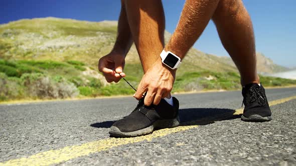 Triathlete man tying his shoe lace in the countryside road