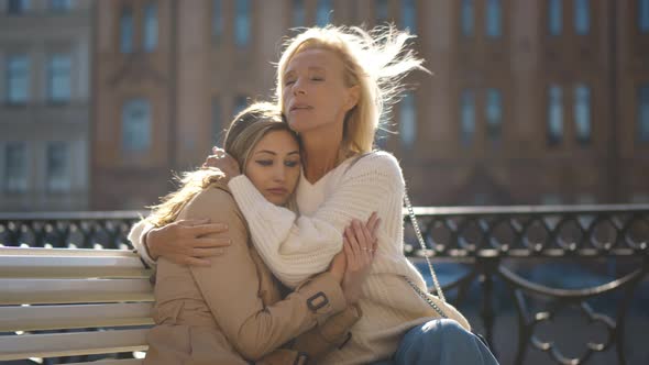 Daughter with Senior Mother Sitting on City Bench and Hugging