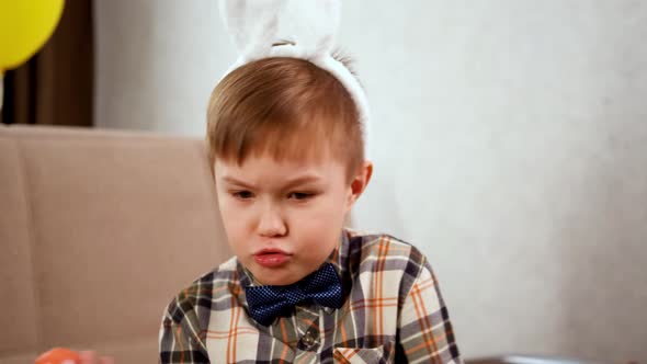 A Boy in White Bunny Ears Holds an Orange Egg in His Hands