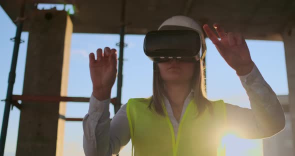 A Woman Engineer at a Construction Site in Virtual Reality Glasses Moves Her Hands Simulating the