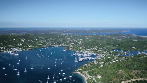 Aerial shot of the bay with white yachts, a city and a dense forest in Antigua and Barbuda