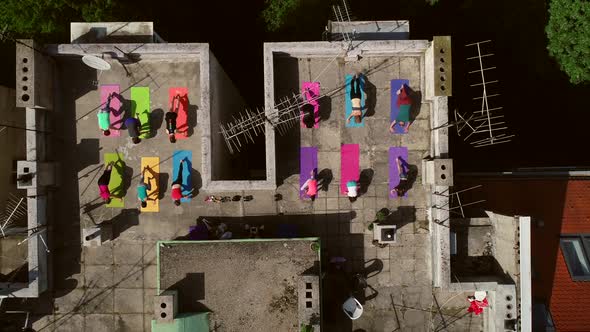 Aerial view of a group of people doing yoga on a rooftop at the city in summer.