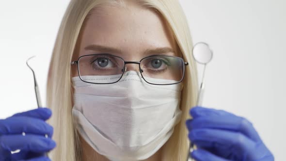 Woman Dentist in Mask and Glasses on White Background with Dental Instruments
