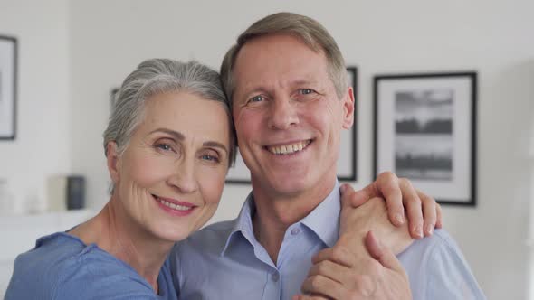 Happy Senior Mature 60s Family Couple Hugging Looking at Camera at Home