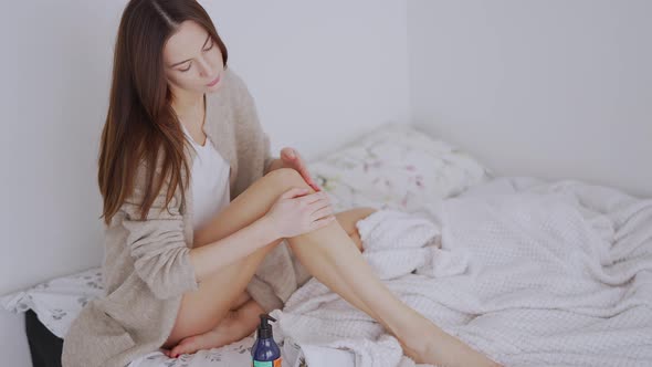 Woman Smearing Cream on Leg on Bed