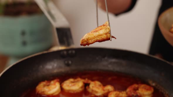 Chef using a cooking tweezer, grip, lift and transfer the cooked shrimps from frying pan into a bowl