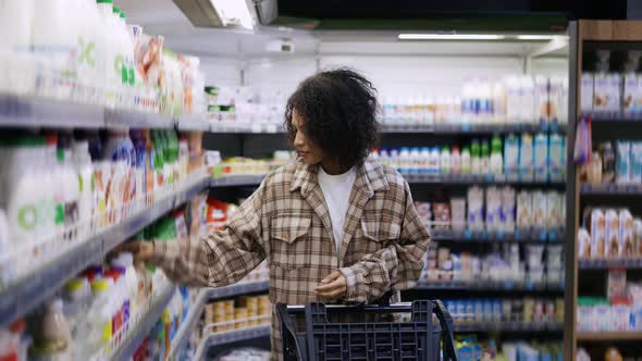 Positive Black Woman with Mobile Device and Trolley Purchasing Products at Mall