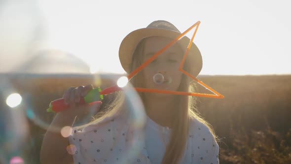 Little Girl Blowing Soap Bubbles in Wheat Field at Sunset Time. Slow Motion Video.