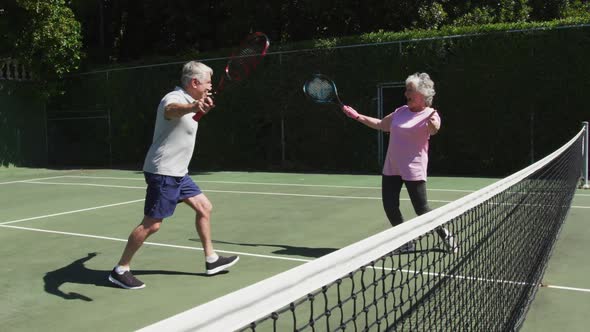 Happy caucasian senior couple embracing on outdoor tennis court in sun after playing a game