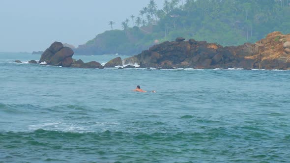 Woman Catches Wave Standing on Surfboard Against Landscape