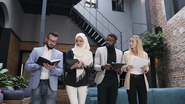 Multiracial Business People Going through the Office Room and Holding in their Hands Documents